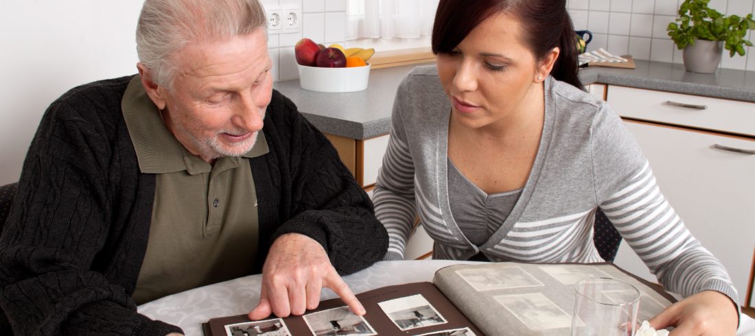 Adulto mayor mirando un album de fotos junto a mujer joven