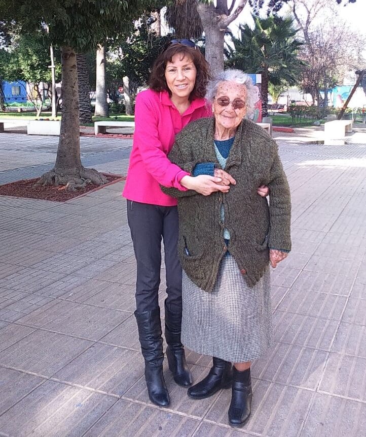 mujer junto a adulta mayor sonriendo en una plaza