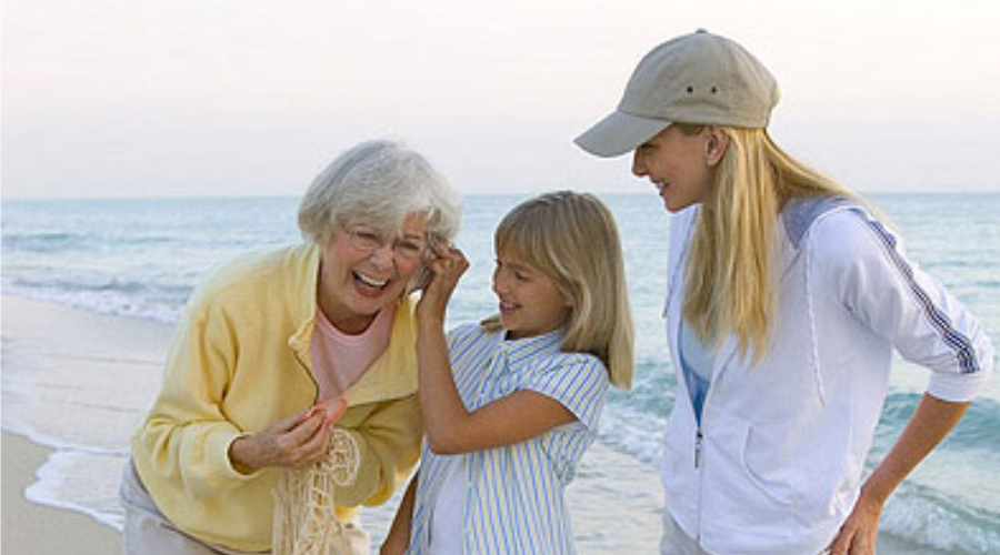 Mujer mayor con su hija y nieta riendo en la playa