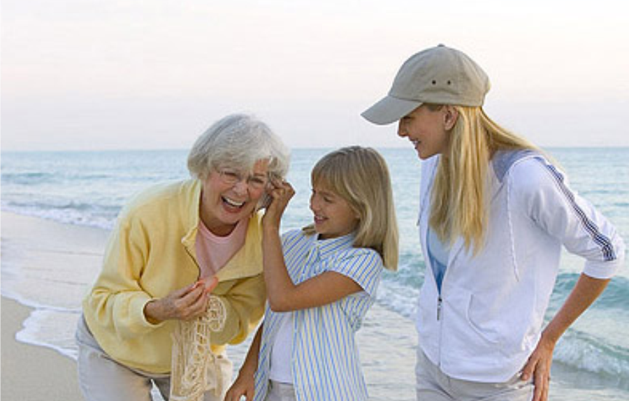 Mujer mayor con su hija y nieta riendo en la playa