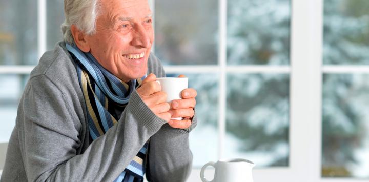 Adulto mayor sonriendo mientras sostiene una taza con ambas manos