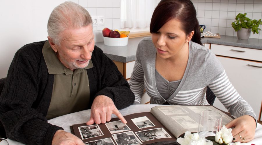 Adulto mayor mirando un album de fotos junto a mujer joven