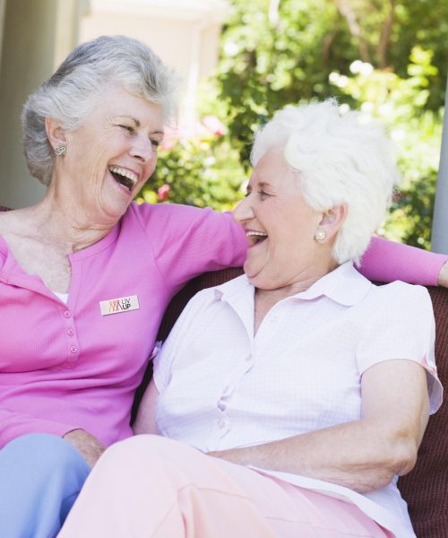 Pareja de adultas mayores riendo sentadas en una banca en el jardín