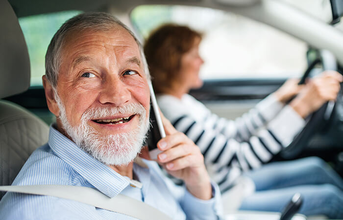 foto de adulto mayor sonriendo al teléfono mientras va en auto de acompañante